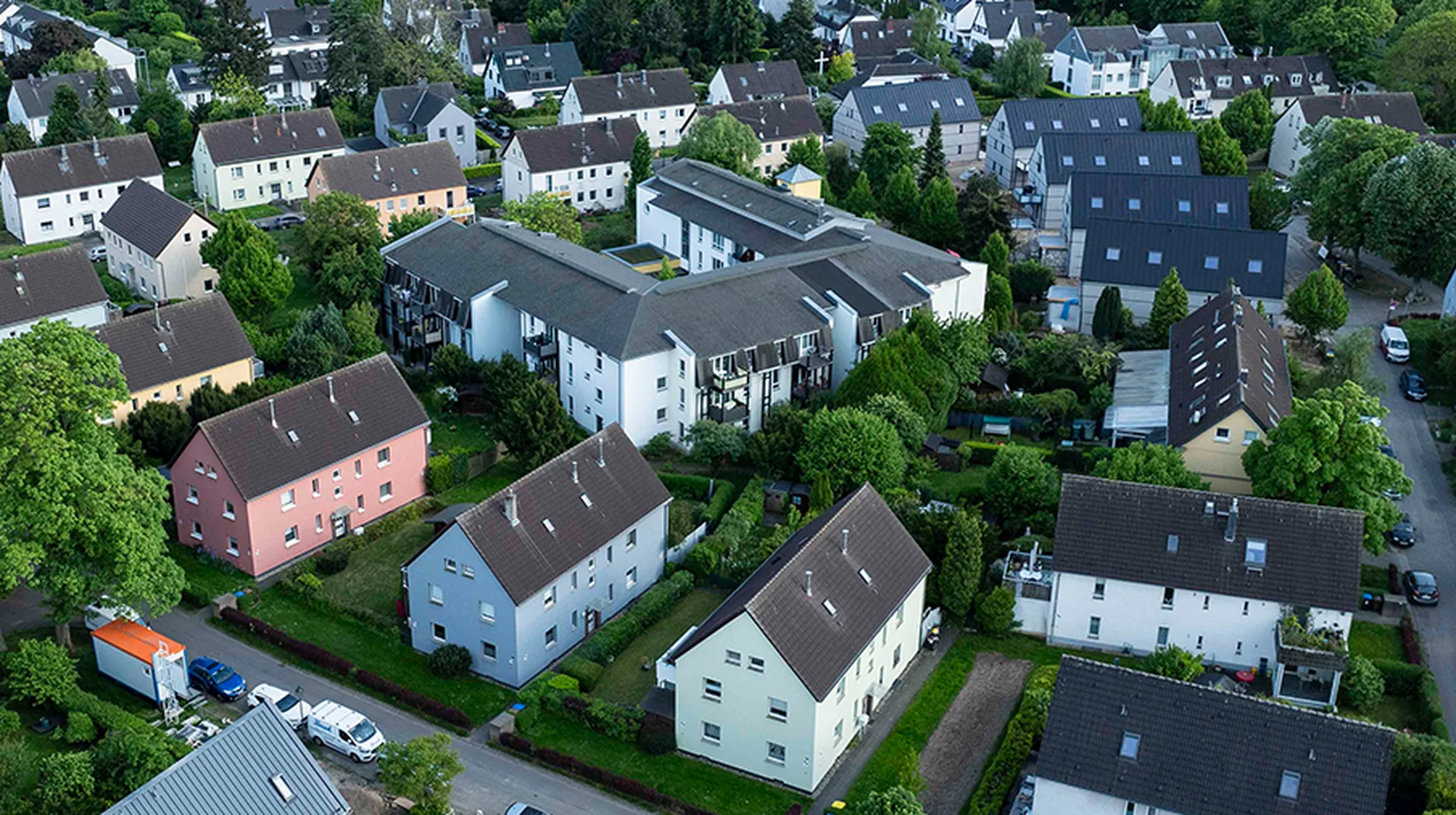 Aerial view of a suburban neighborhood with rows of houses, green lawns, and tree-lined streets on a clear day.