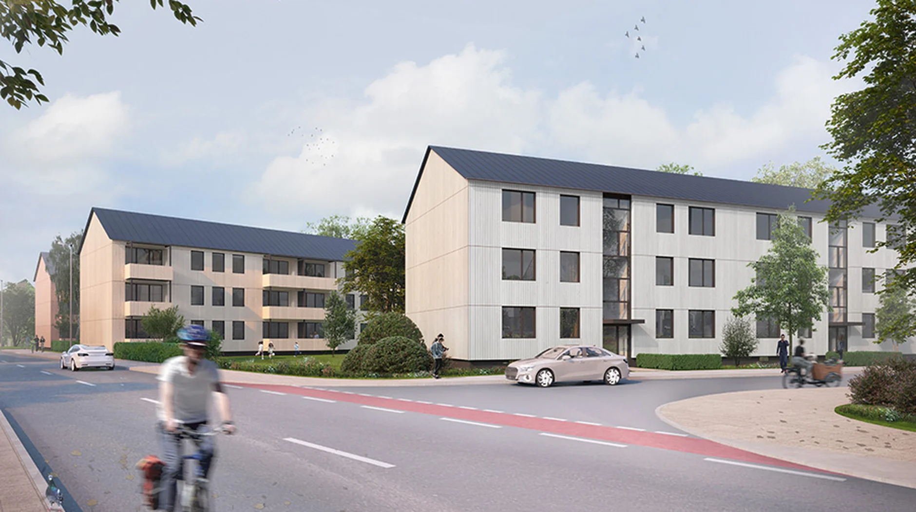 Modern apartment buildings with sloped roofs alongside a road. Cyclist and pedestrians are visible under a partly cloudy sky.
