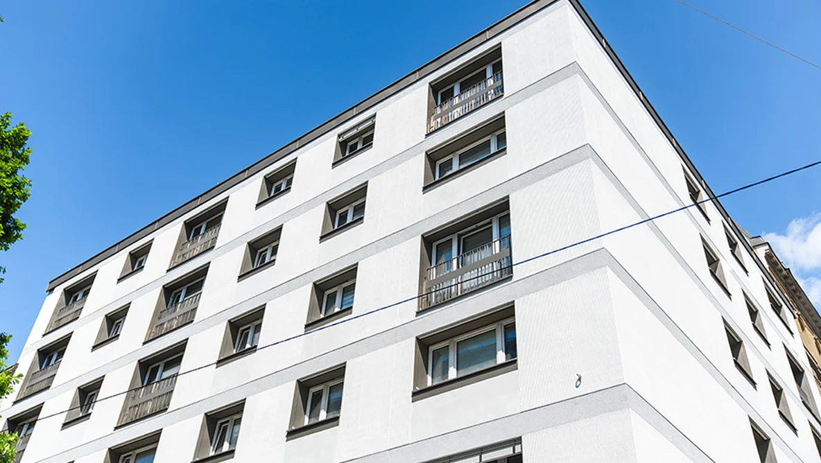 Corner view of a modern white apartment building with multiple windows against a clear blue sky.