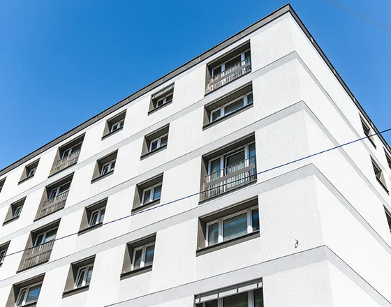 Corner view of a modern white apartment building with multiple windows against a clear blue sky.