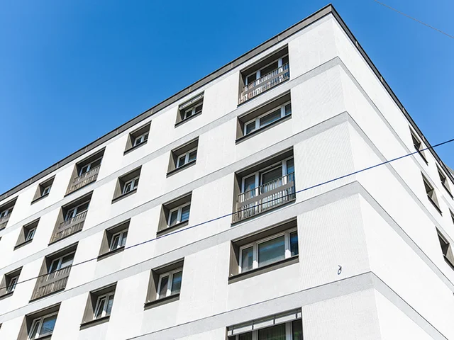 Corner view of a modern white apartment building with multiple windows against a clear blue sky.