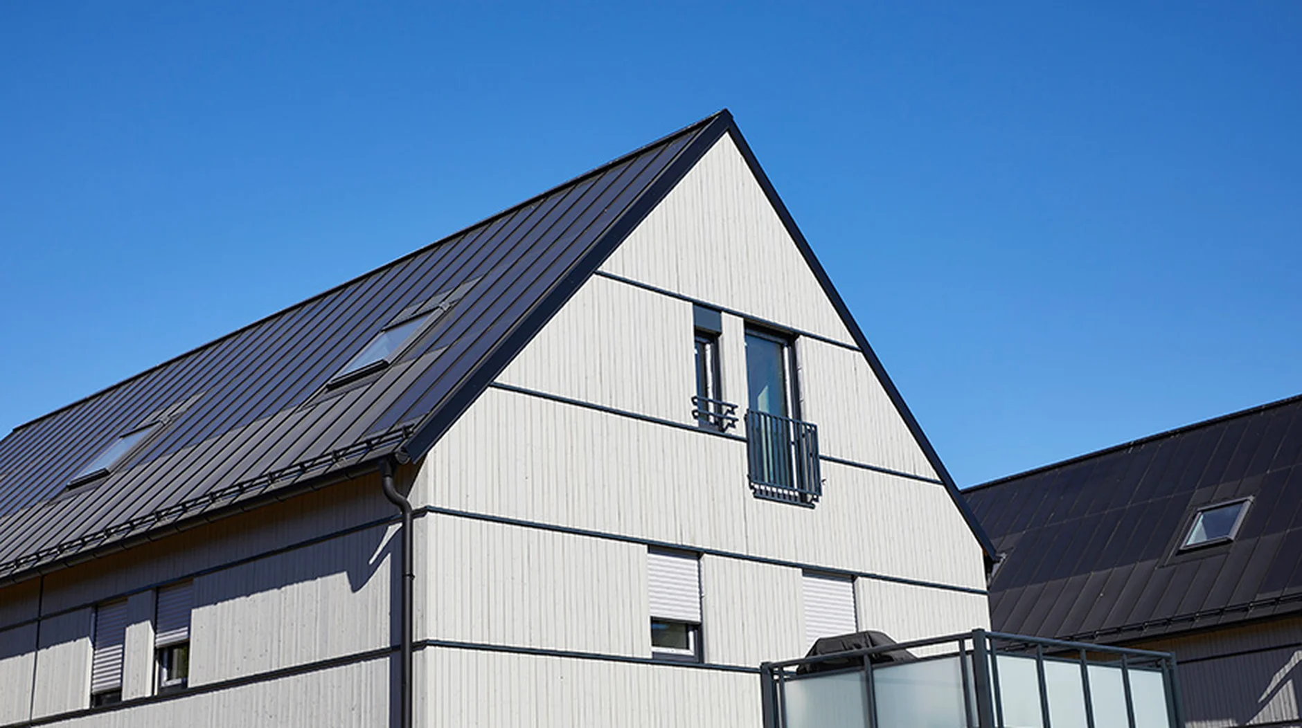 Energieeffizient saniertes Mehrfamilienhaus mit moderner Holzfassade und dunklem Metalldach vor blauem Himmel