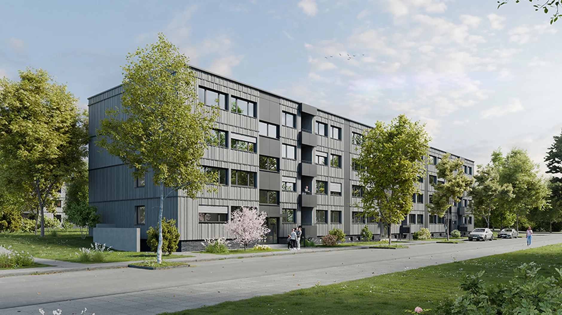 Modern apartment building with gray facade, surrounded by trees and greenery. A sidewalk and parked cars line the street under a partly cloudy sky.