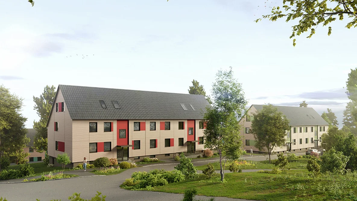 Modern, two-story apartment buildings with dark roofs and light exteriors, surrounded by greenery and a paved walkway under a clear sky.