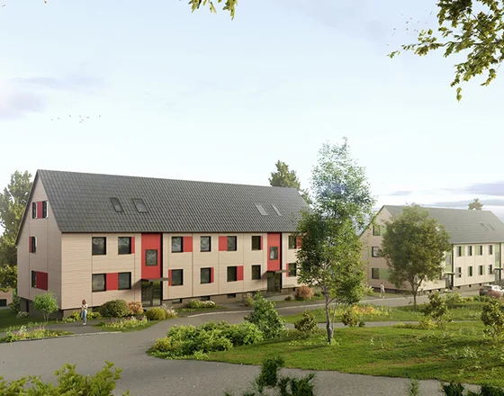 Modern, two-story apartment buildings with dark roofs and light exteriors, surrounded by greenery and a paved walkway under a clear sky.