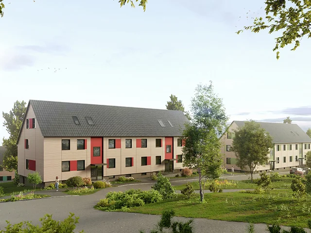 Modern, two-story apartment buildings with dark roofs and light exteriors, surrounded by greenery and a paved walkway under a clear sky.